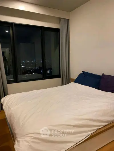 Cozy bedroom with city view, featuring a comfortable bed and large window.