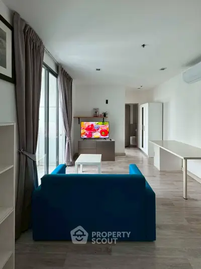 Modern living room with blue sofa, wall-mounted TV, and large windows for natural light.