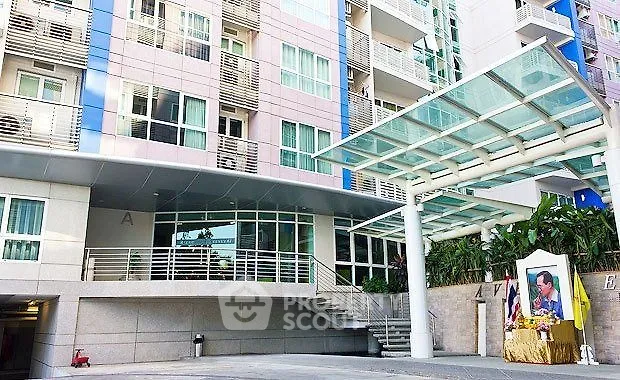 Modern apartment building entrance with glass canopy and landscaped surroundings.