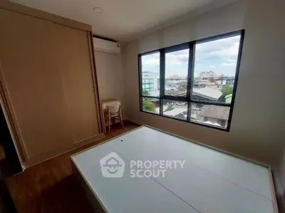 Modern bedroom with large window offering city view, featuring built-in wardrobe and compact workspace.