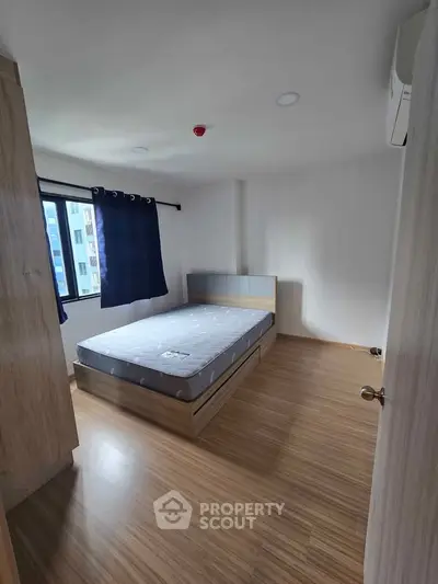 Spacious bedroom with wooden flooring and large window in modern apartment.