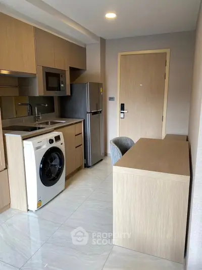 Modern kitchen with washing machine, fridge, and microwave in compact apartment.