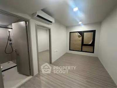Modern unfurnished apartment with air conditioning and wooden flooring, featuring a bathroom and large window.
