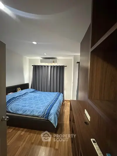 Cozy bedroom with wooden flooring and modern furnishings, featuring a comfortable bed and ample natural light.