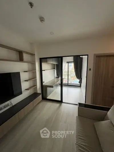 Modern living room with sliding glass doors leading to a bright study area, featuring sleek shelving and a wall-mounted TV.
