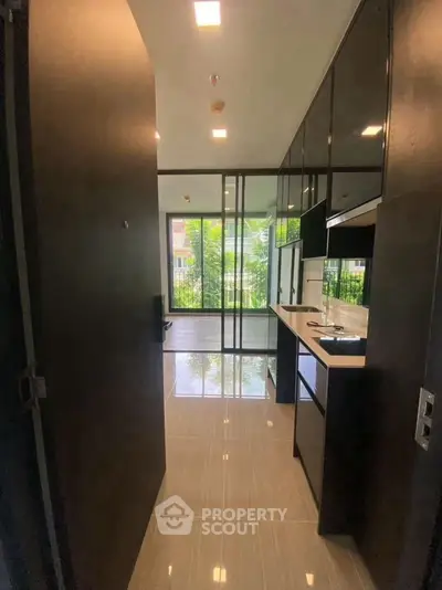 Modern kitchen with sleek black cabinets and large windows offering garden view.