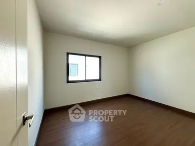 Spacious empty bedroom with wooden flooring and large window, perfect for customization.