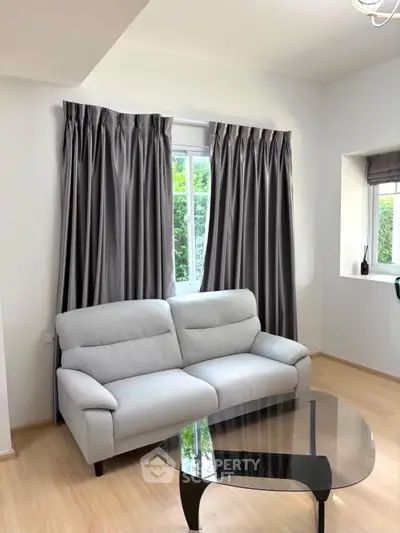 Modern living room with sleek gray sofa and glass coffee table, featuring elegant curtains and natural light.