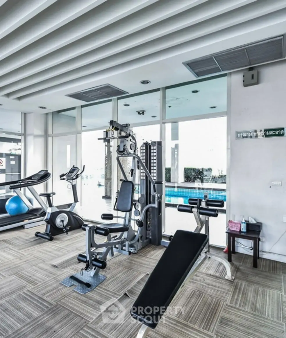 Modern gym with exercise equipment and pool view in luxury apartment complex.