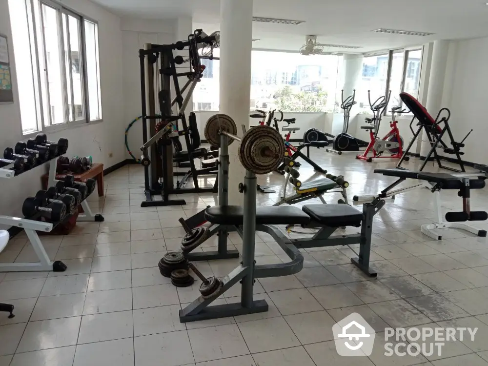 Spacious gym with modern fitness equipment and large windows for natural light.