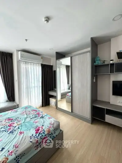 Modern bedroom with floral bedding, mirrored wardrobe, and natural light from large windows.