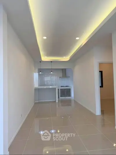 Modern open-plan kitchen and living area with sleek lighting and tiled flooring.
