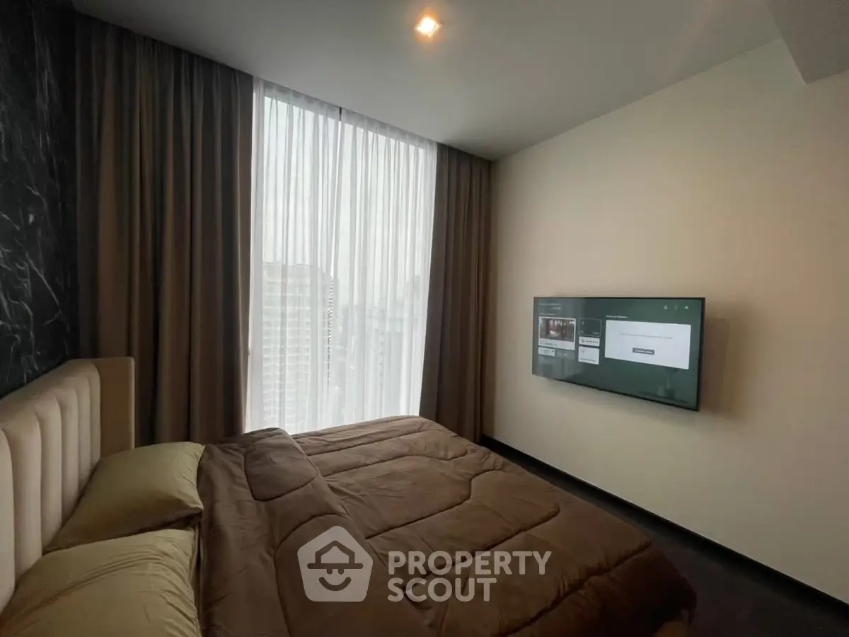 Modern bedroom with large window and wall-mounted TV in high-rise apartment.