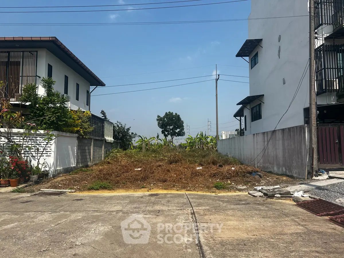 Vacant land plot between two modern houses, ideal for new construction in a residential area.