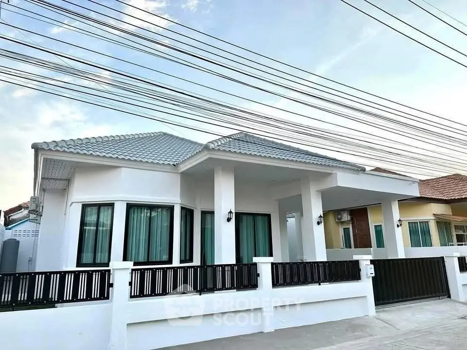 Modern single-story house with white facade and black fence, showcasing contemporary architecture.