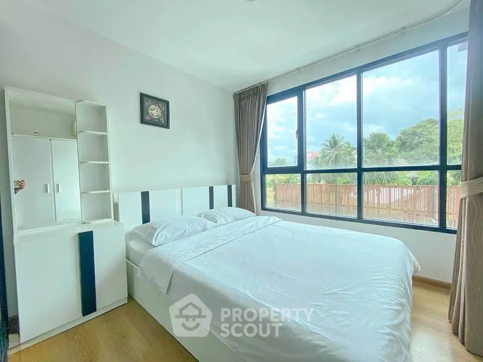 Bright and airy bedroom with large windows and modern furnishings, offering a serene view of lush greenery.