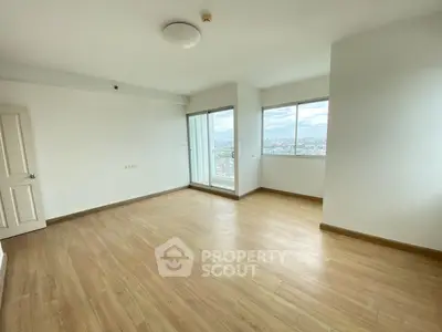 Spacious empty room with wooden flooring and large windows offering city views.