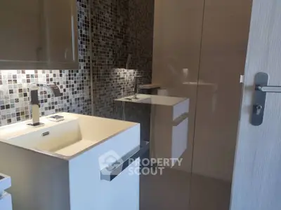 Modern bathroom with sleek design, featuring mosaic tiles, a large mirror, and minimalist white cabinetry for a clean aesthetic.