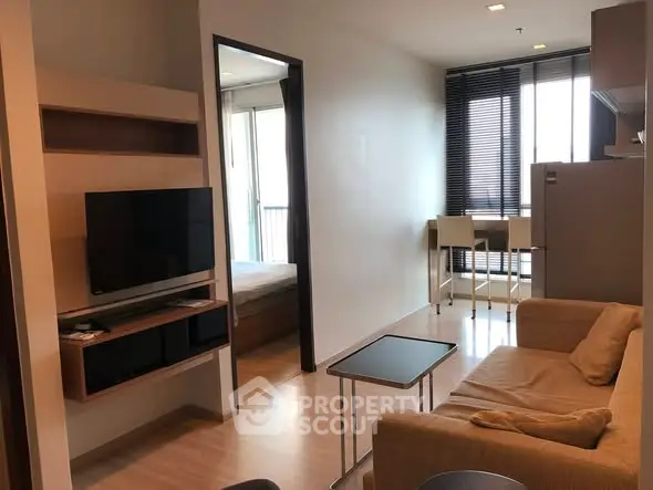 Modern apartment living room with cozy sofa, wall-mounted TV, and natural light from large windows.