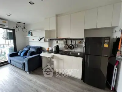 Modern living room with compact kitchen and balcony view, featuring sleek cabinetry and stylish decor.