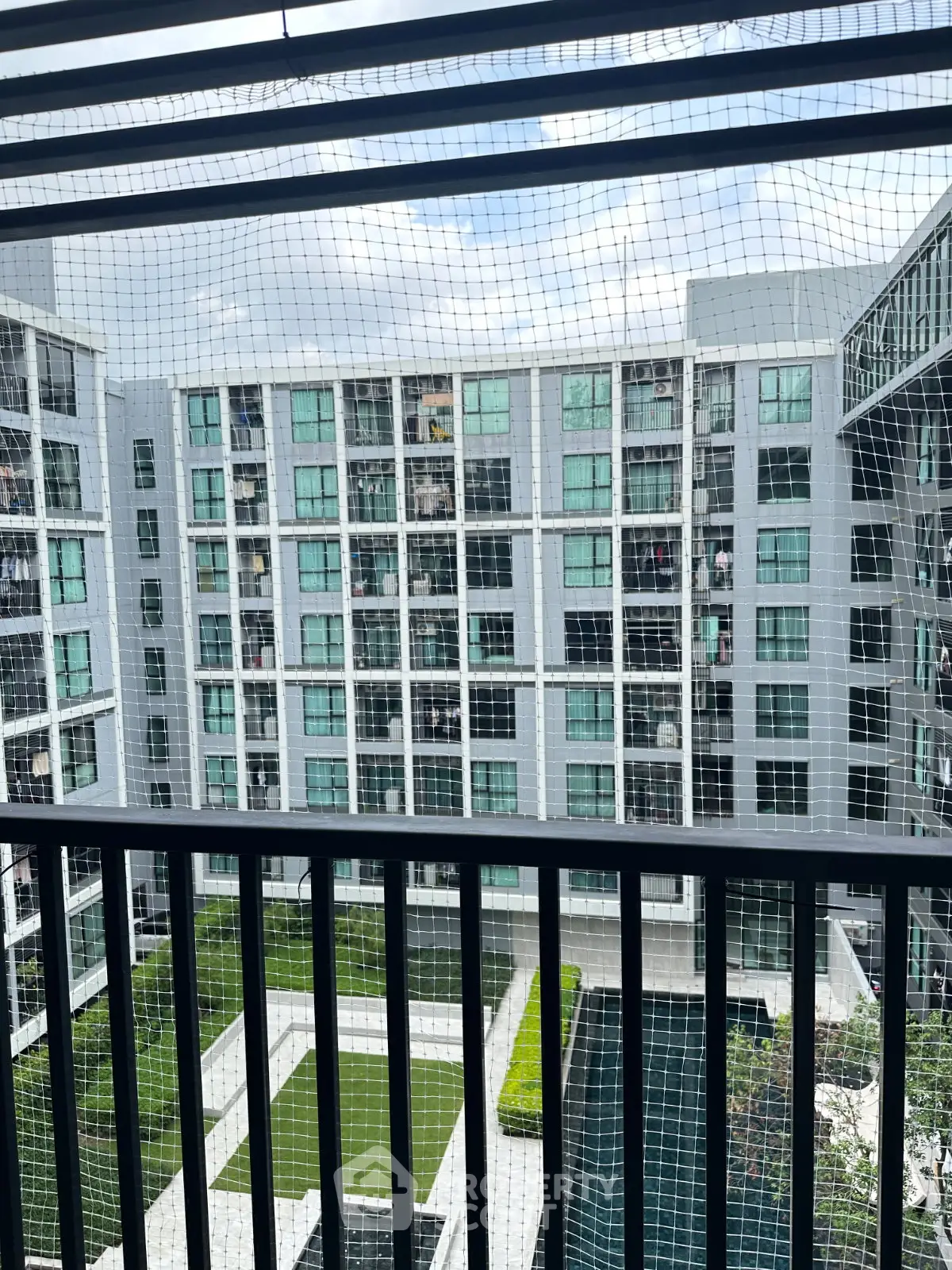 Modern apartment complex with pool view from balcony, showcasing sleek architecture and lush greenery.