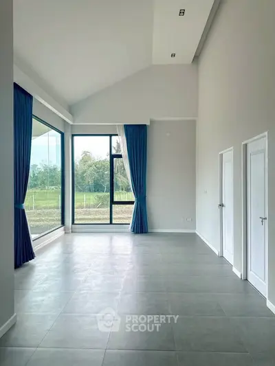 Spacious modern living room with large windows and blue curtains, offering a serene view.