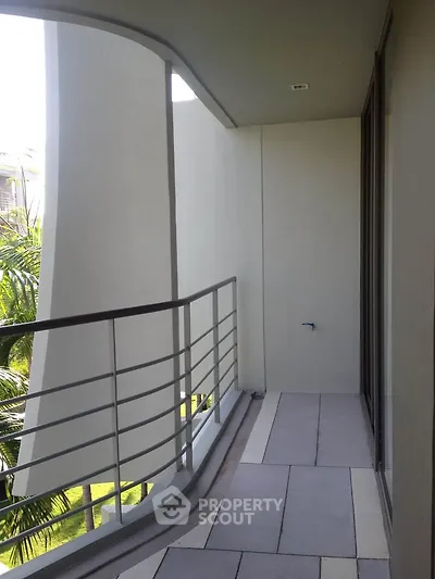 Modern apartment balcony with sleek railing and lush greenery view.