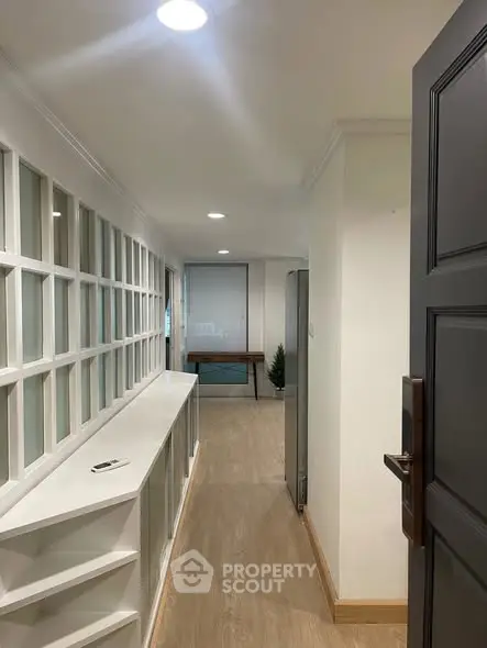 Modern hallway with wooden flooring and built-in shelving, leading to a bright room.