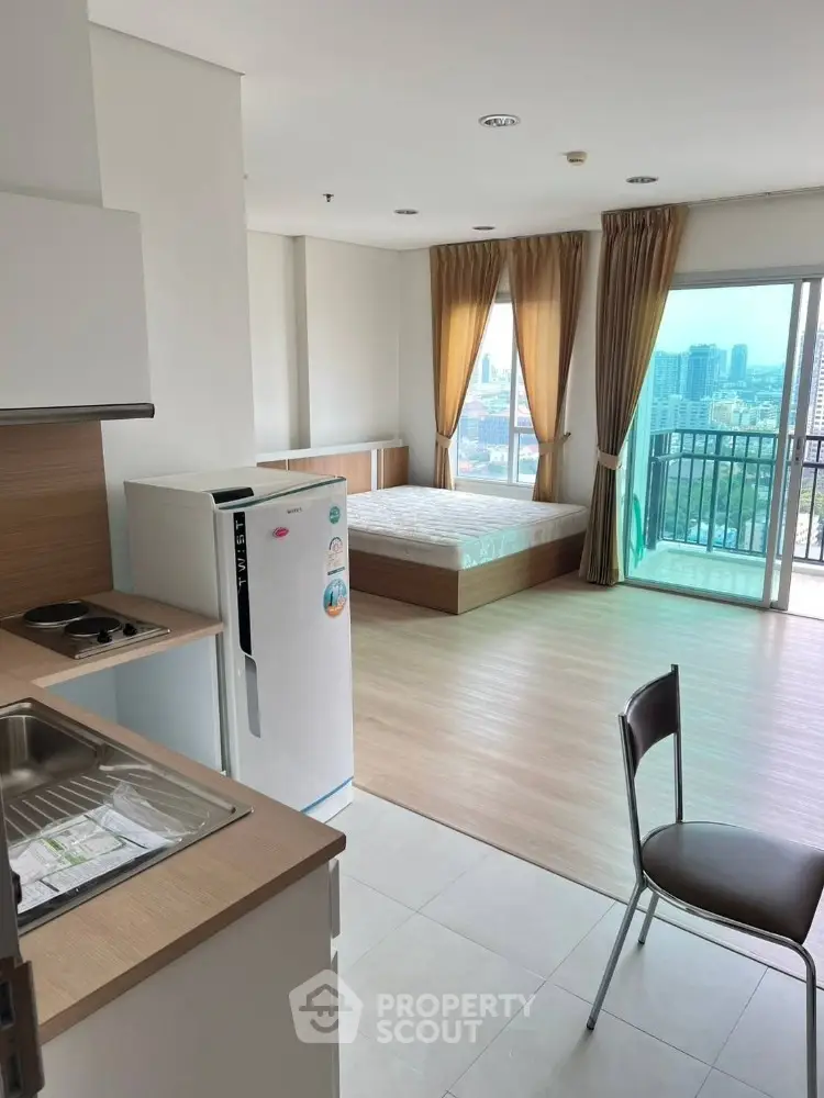 Modern studio apartment with city view, featuring compact kitchen and cozy bedroom area.