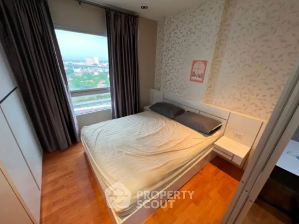 Cozy bedroom with large window offering city view, featuring modern decor and wooden flooring.