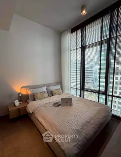 Modern bedroom with large windows and city view, featuring a cozy bed and stylish decor.