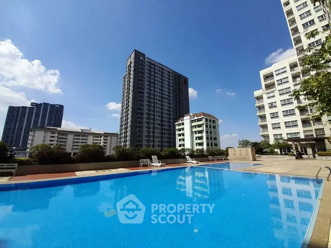 Luxurious high-rise condominium complex with a sparkling outdoor pool under a clear blue sky, offering urban living with top-notch amenities.