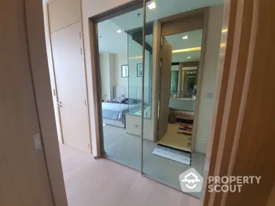 Modern apartment hallway leading to a cozy bedroom with mirrored closet doors.