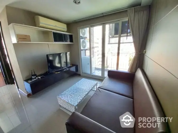 Sunlit cozy living room with modern furnishings, featuring a comfortable brown sofa, sleek TV unit, and balcony access for an airy ambiance.