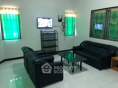 Cozy living room with black leather sofas, glass coffee table, and wall-mounted TV, perfect for relaxation.