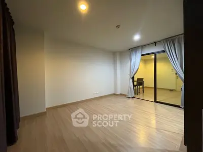 Spacious empty room with wooden flooring and sliding glass doors leading to a balcony.