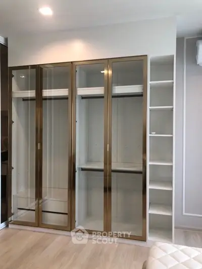 Modern built-in wardrobe with glass doors and shelving in a stylish bedroom.