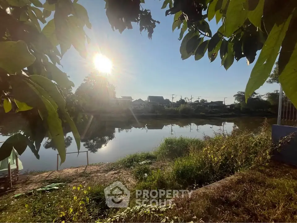 Serene riverside view with lush greenery and distant houses under a bright sun.