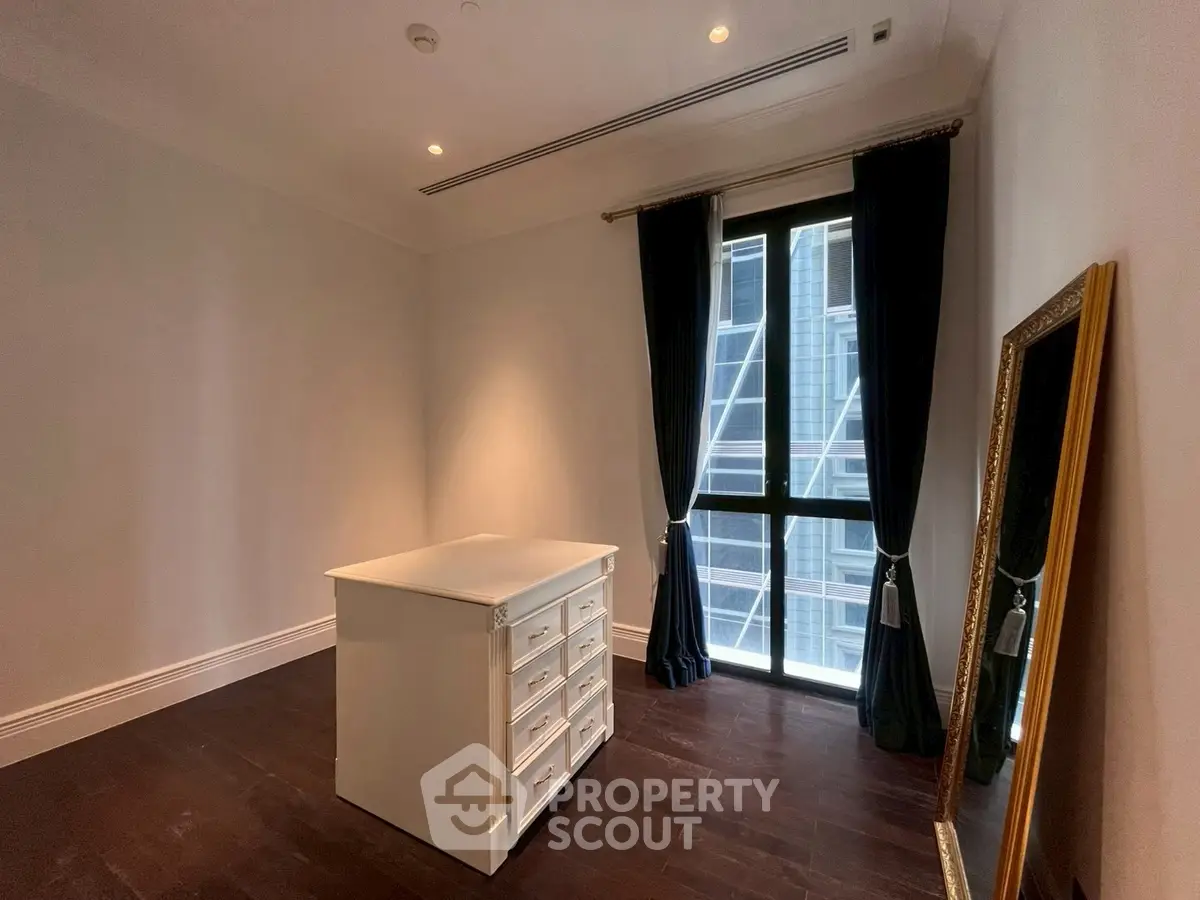 Spacious room with elegant dark flooring and large window, featuring a stylish dresser and full-length mirror.