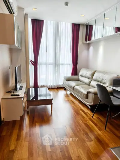 Modern living room with wooden flooring, sleek furniture, and large windows with red curtains.