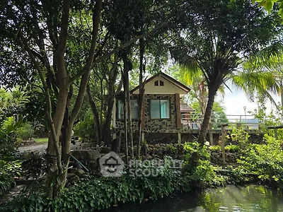 Charming stone cottage surrounded by lush greenery and tranquil pond view.