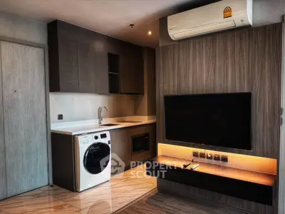 Modern living room with sleek kitchen, washing machine, and mounted TV in stylish apartment.