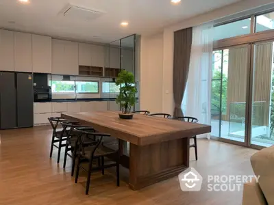 Spacious modern kitchen with sleek cabinetry and integrated appliances, complemented by a large dining table and access to a sunlit balcony.