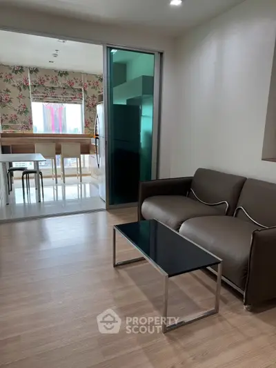 Modern living room with sleek sofa and glass coffee table, adjacent to a stylish kitchen with floral wallpaper.
