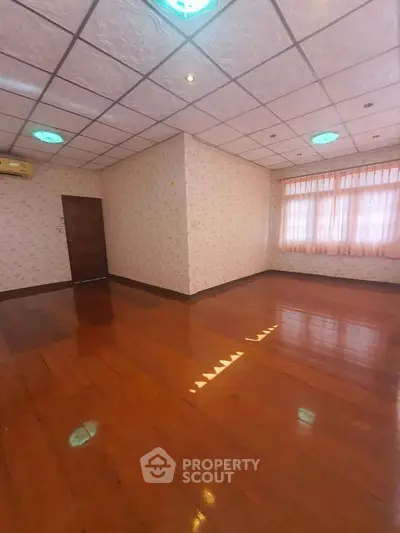 Spacious empty room with wooden flooring and large windows, perfect for customization.