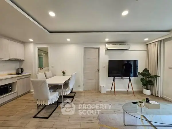 Modern open-plan living room with dining area and sleek kitchen, featuring a wall-mounted TV and stylish decor.