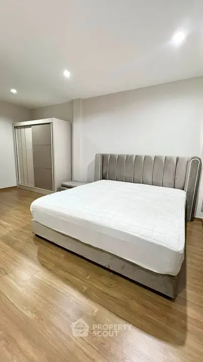 Spacious modern bedroom with elegant bed and sleek wardrobe on wooden flooring.