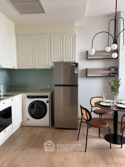 Modern kitchen with sleek appliances and dining area, featuring a washing machine and stylish lighting.