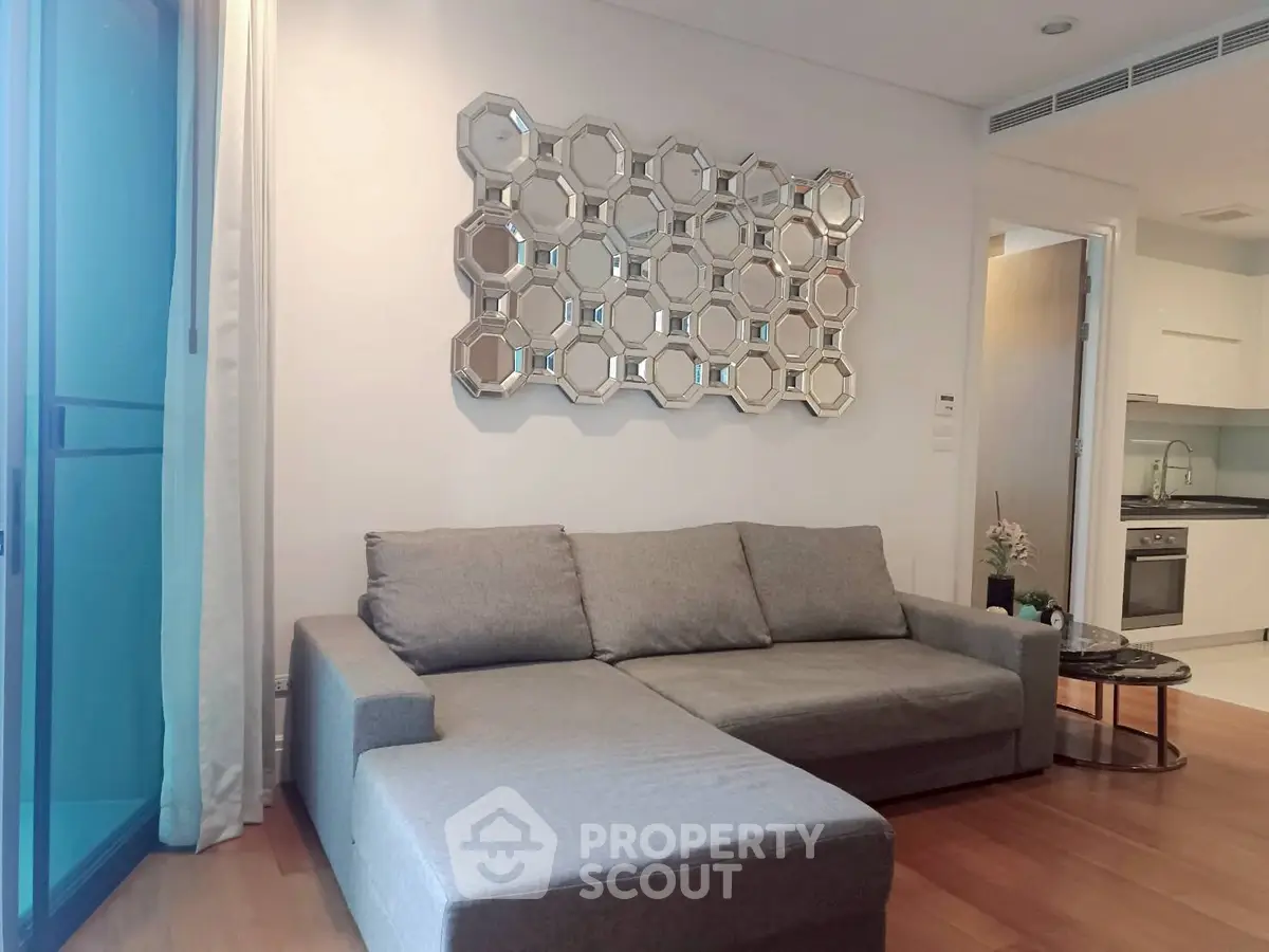 Modern living room with stylish sofa and decorative mirror, adjacent to a sleek kitchen area.