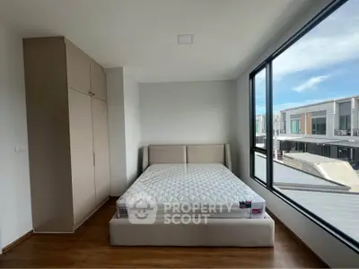 Modern bedroom with large window and wardrobe, offering natural light and urban view.